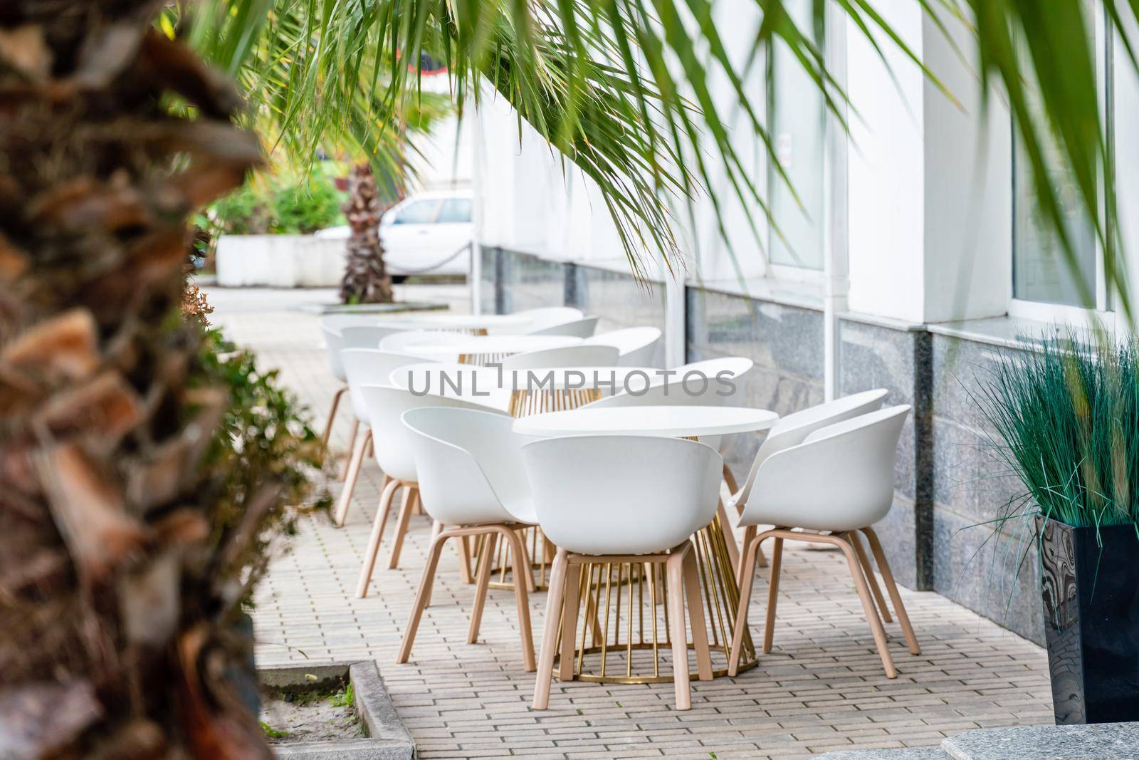 Street cafe with white chairs, green foliage around. Without people, tourism, travel