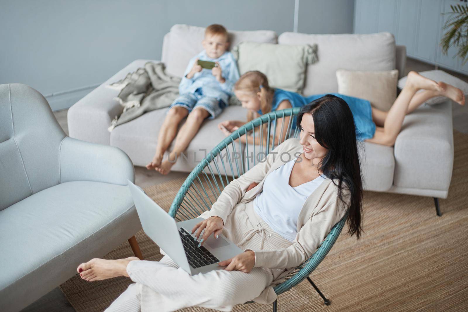 mother is working on a laptop sitting in a cozy armchair . by SmartPhotoLab
