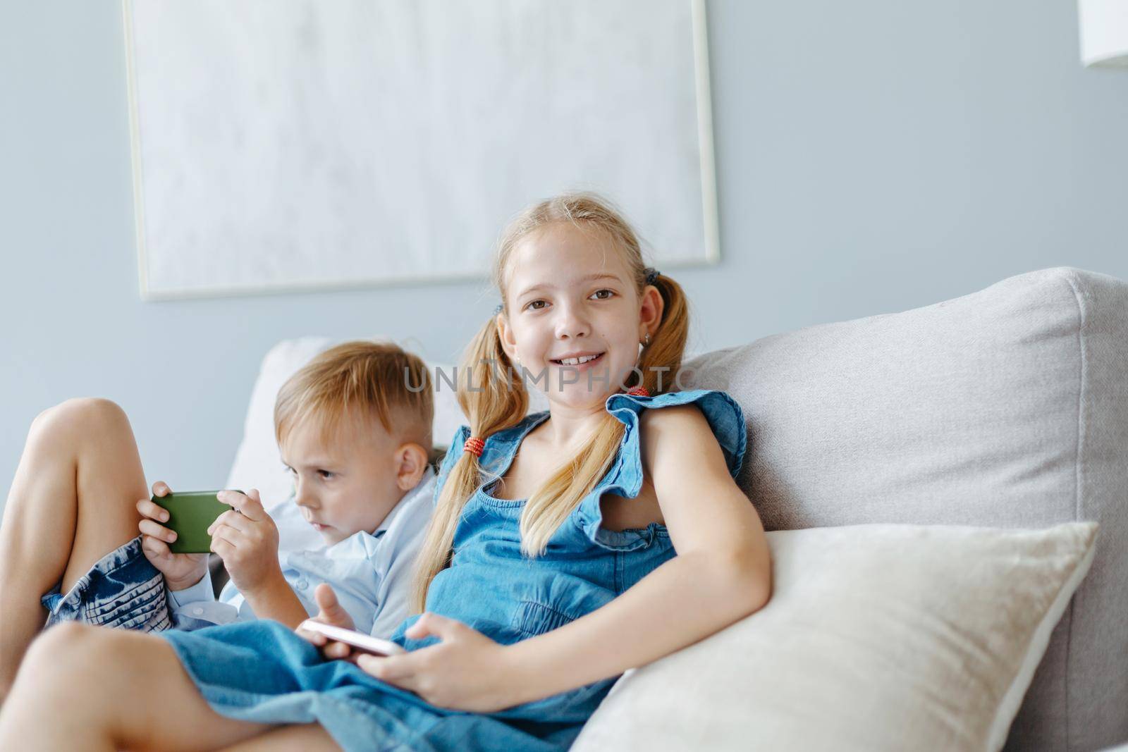 smiling little girl with a smartphone sitting on the couch. by SmartPhotoLab