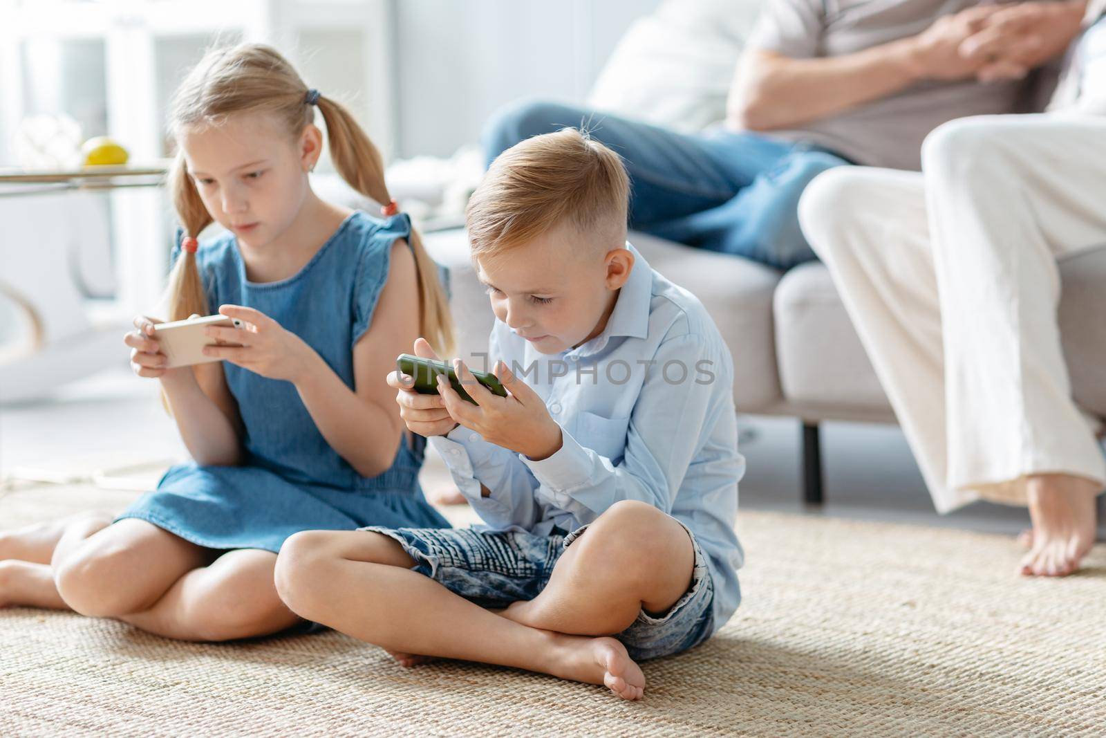 brother and sister with smartphones sitting on the floor in the living room. by SmartPhotoLab