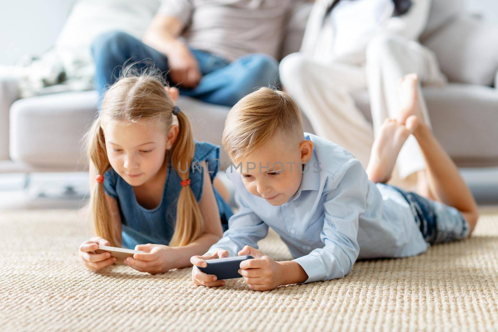 little brother and sister playing entertaining games on their smartphones. by SmartPhotoLab