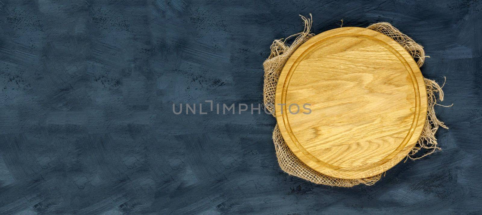 Empty wooden round board on the kitchen black table. Wooden pizza plate, a place to copy. View from above. Mockup. Copy space
