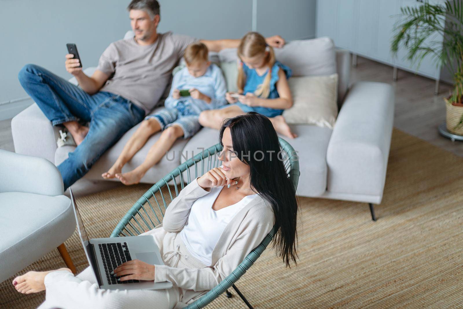 family with their devices spends the evening in a cozy living room . by SmartPhotoLab