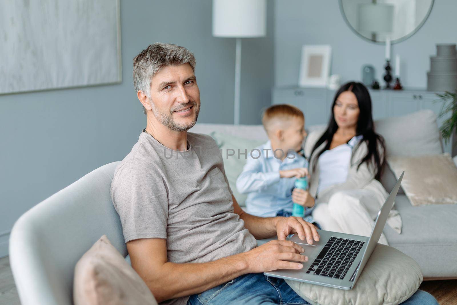 smiling father with a laptop sitting in a cozy living room. by SmartPhotoLab