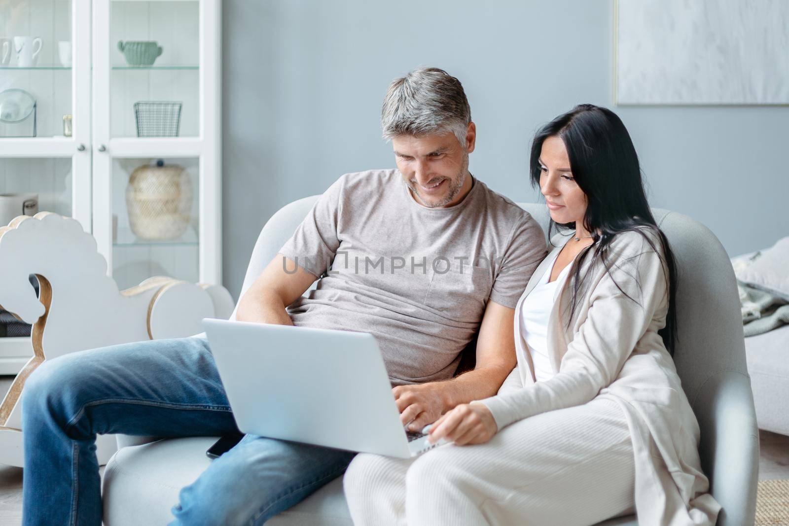 husband and wife using a laptop in their living room. by SmartPhotoLab