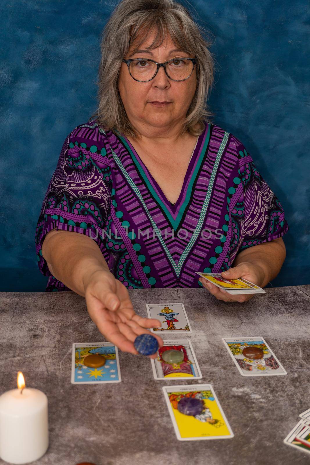 older white-haired woman reading tarot cards on a wooden table with candle