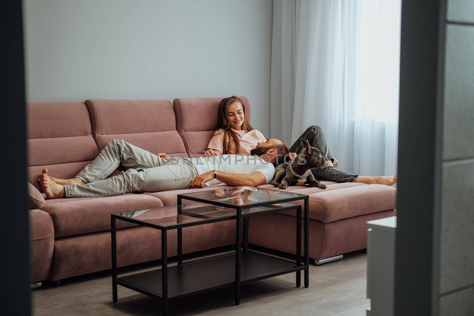 Cheerful Woman and Man Relaxing on Pink Sofa with Pet, Adult Couple Having Leisure with Their French Bulldog at Home