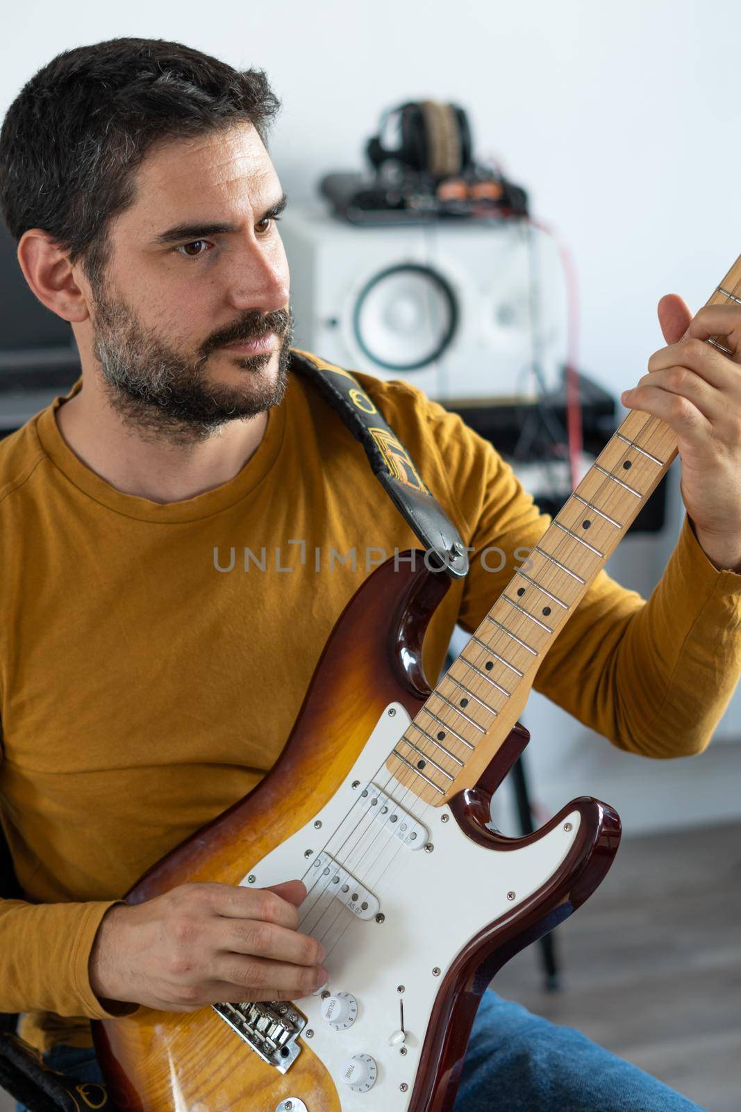 young boy with beard playing guitar at home with piano on the back