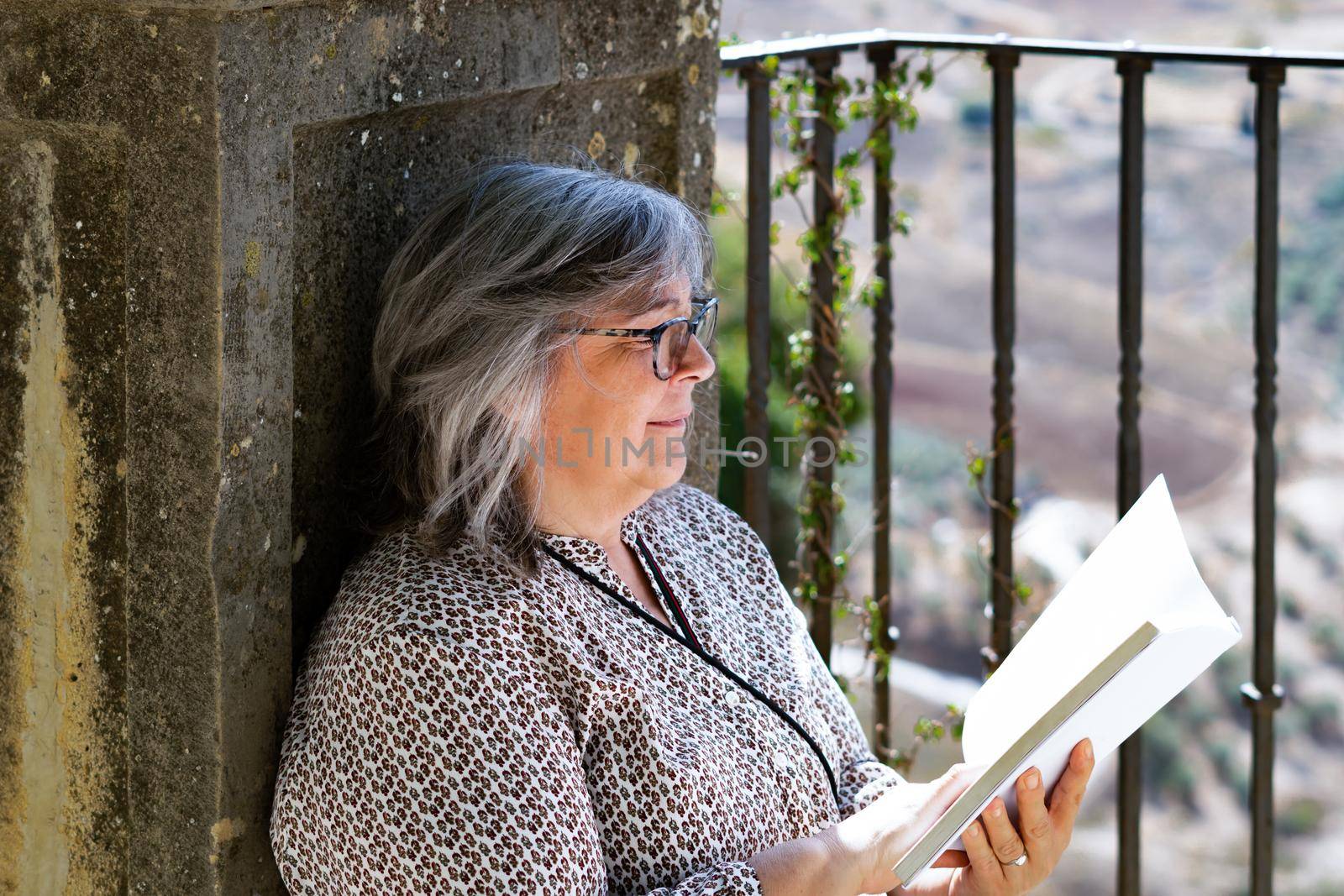 white-haired woman with glasses reading a book in the park
