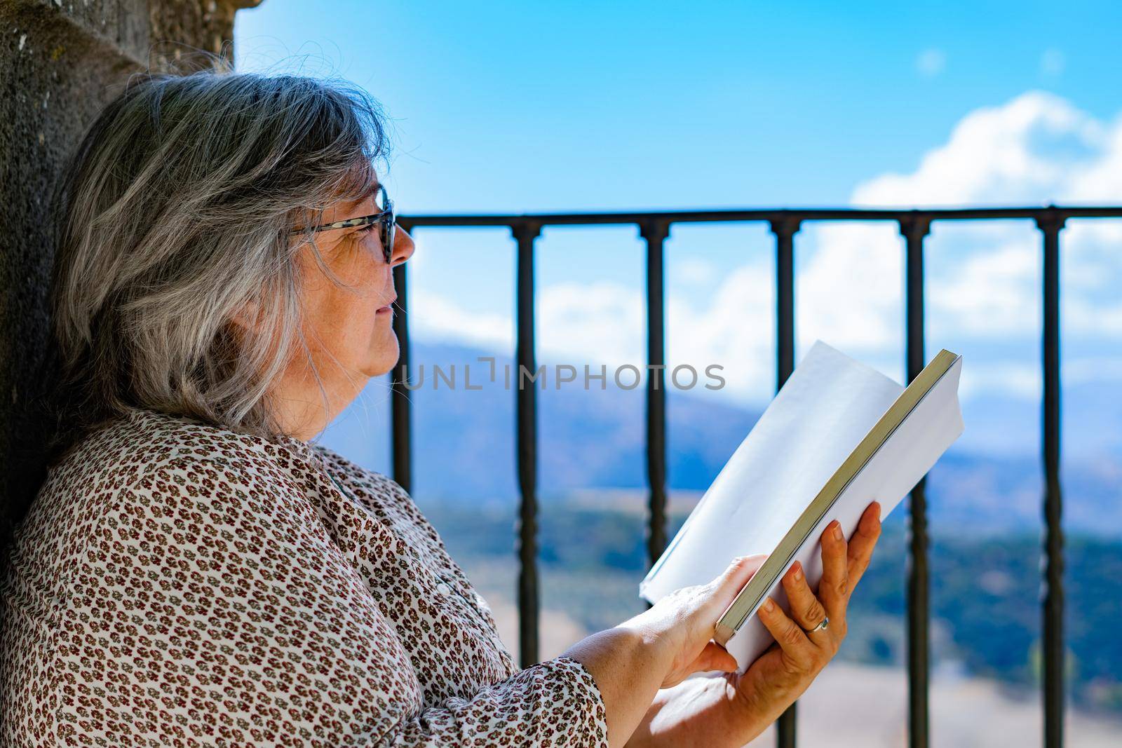 white-haired woman with glasses reading a book in the park