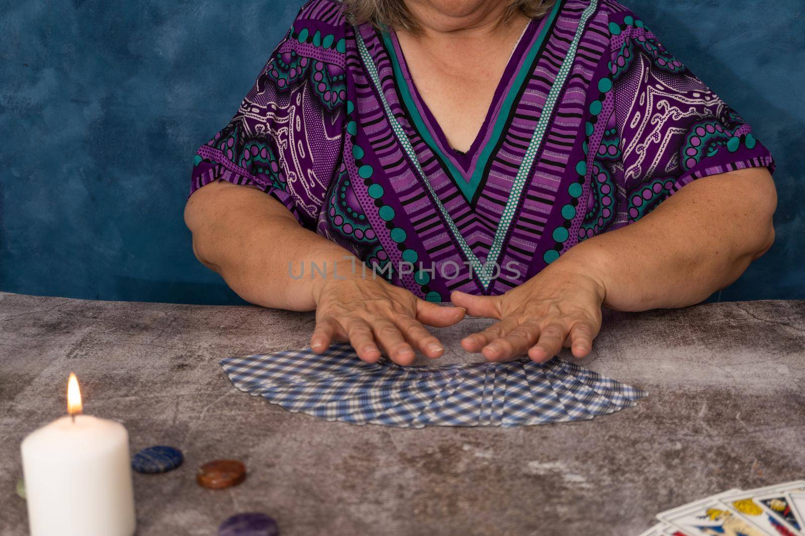 older white-haired woman reading tarot cards on a wooden table with candle