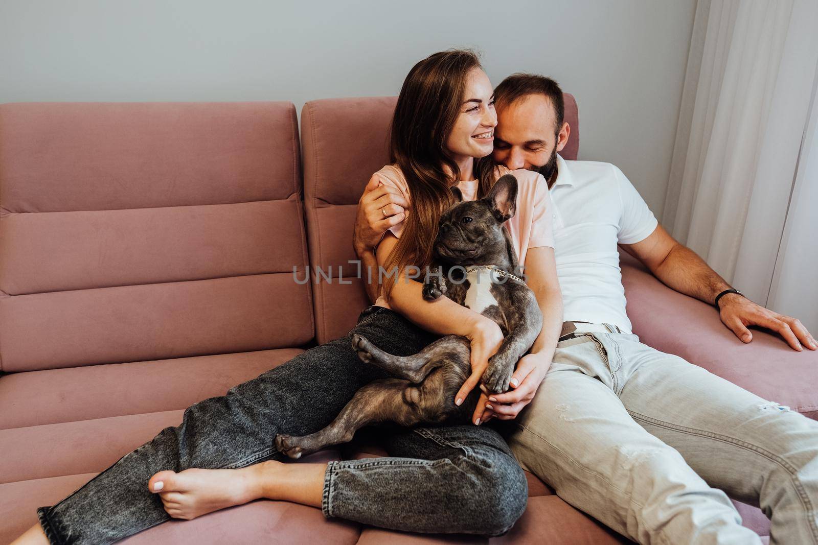 Adult Couple Having Leisure with French Bulldog at Home, Cheerful Woman and Man Relaxing on Pink Sofa with Their Pet