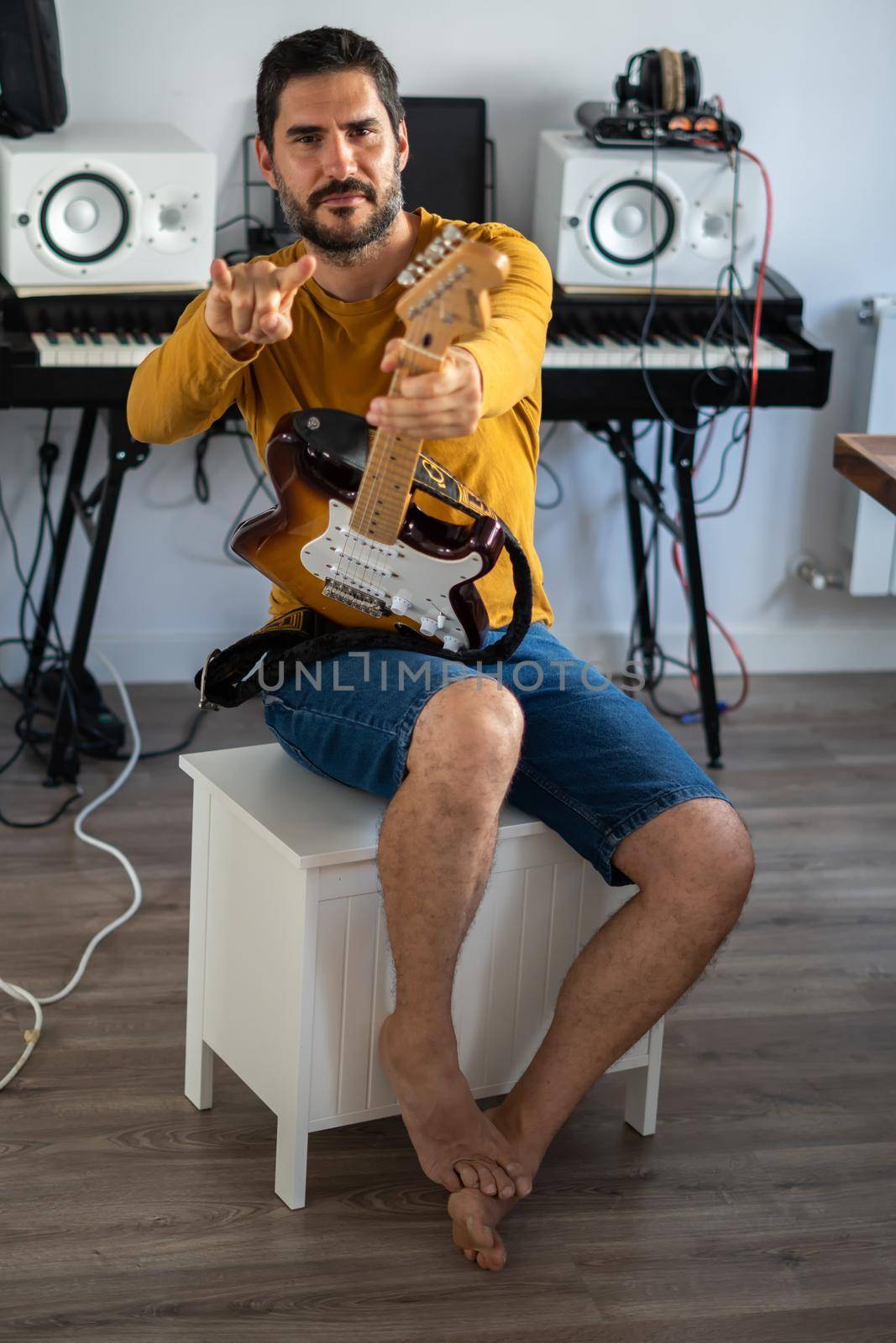 young boy with beard playing guitar at home with piano on the back