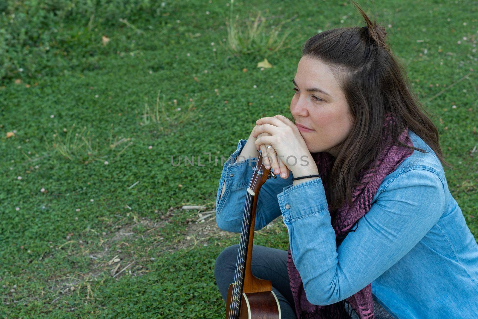 young brunette girl with long hair playing ukulele in the field on the grass