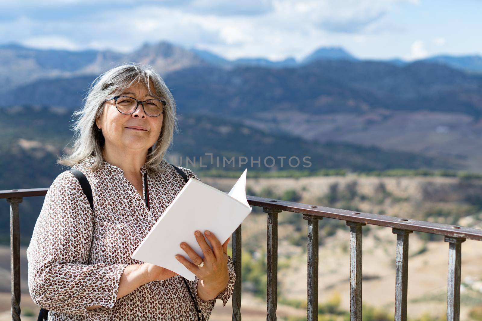 white-haired woman with glasses reading a book in the park