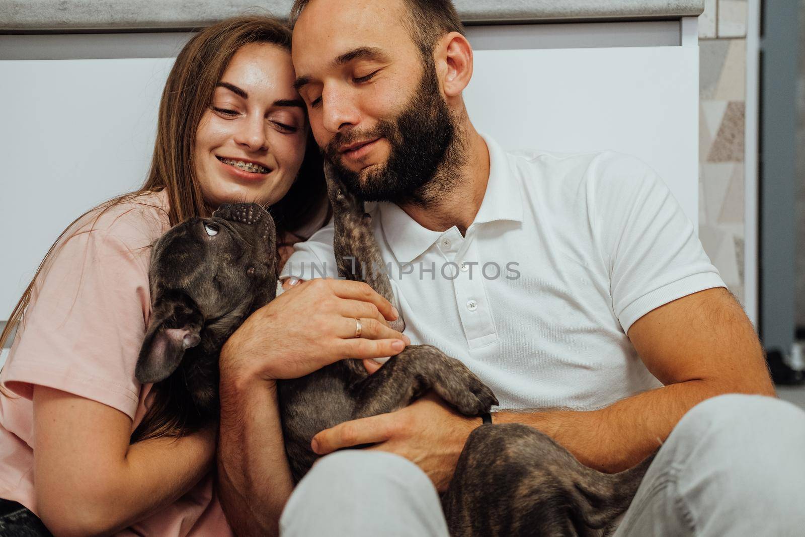 Happy Man and Cheerful Young Woman Hugging with Their Lovely Pet, French Bulldog with His Family at Home