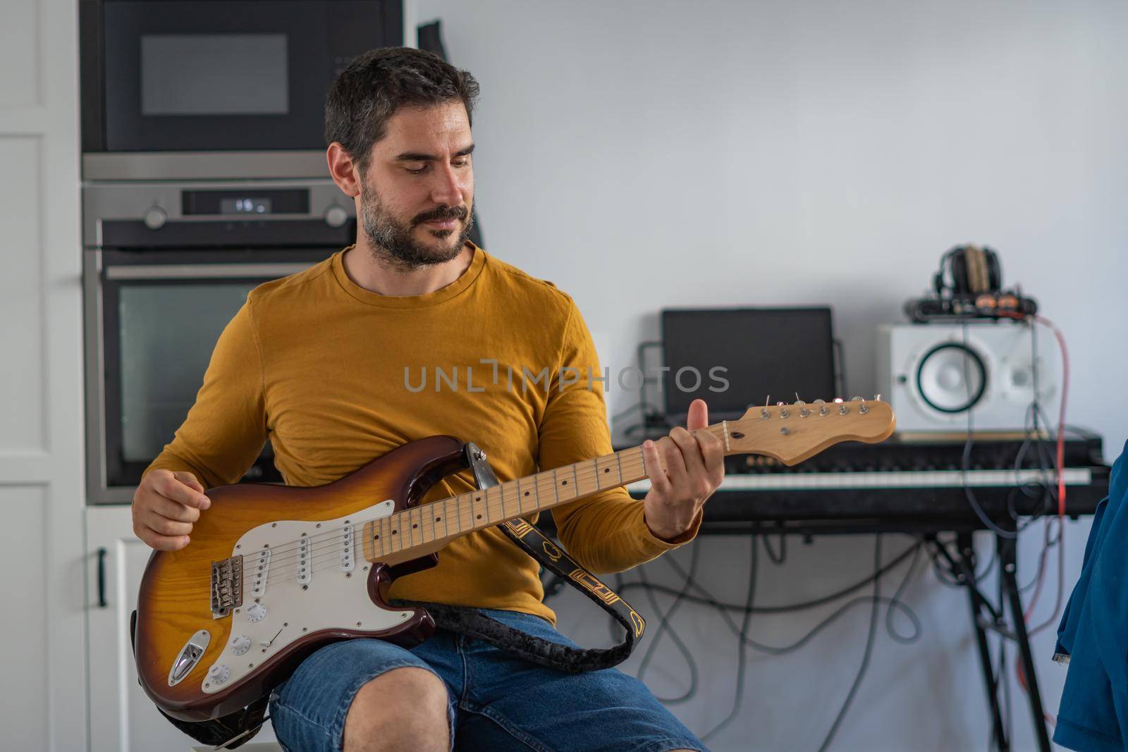 young boy with beard playing guitar at home with piano on the back