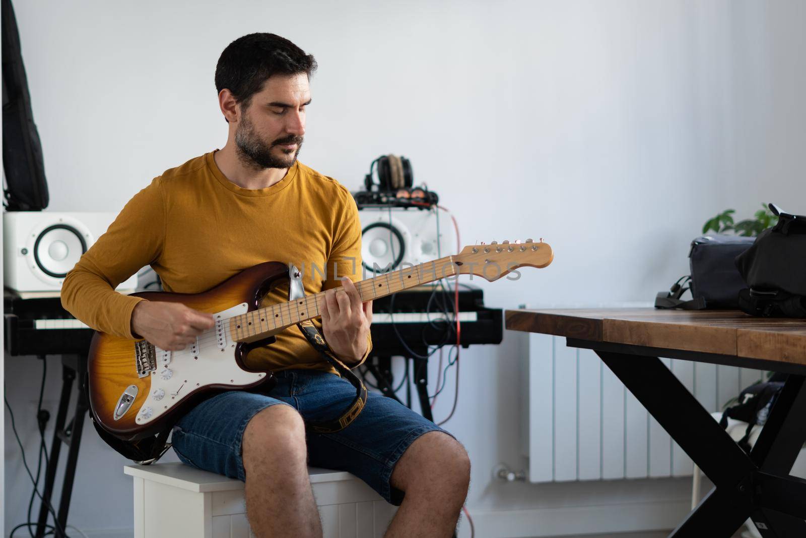 young boy with beard playing guitar at home with piano on the back