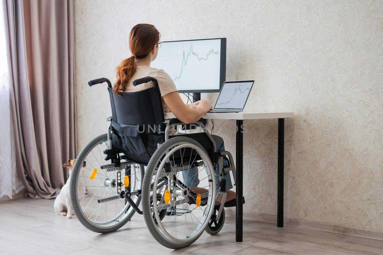 Caucasian woman in a wheelchair typing with a laptop from home. Remote work for people with disabilities