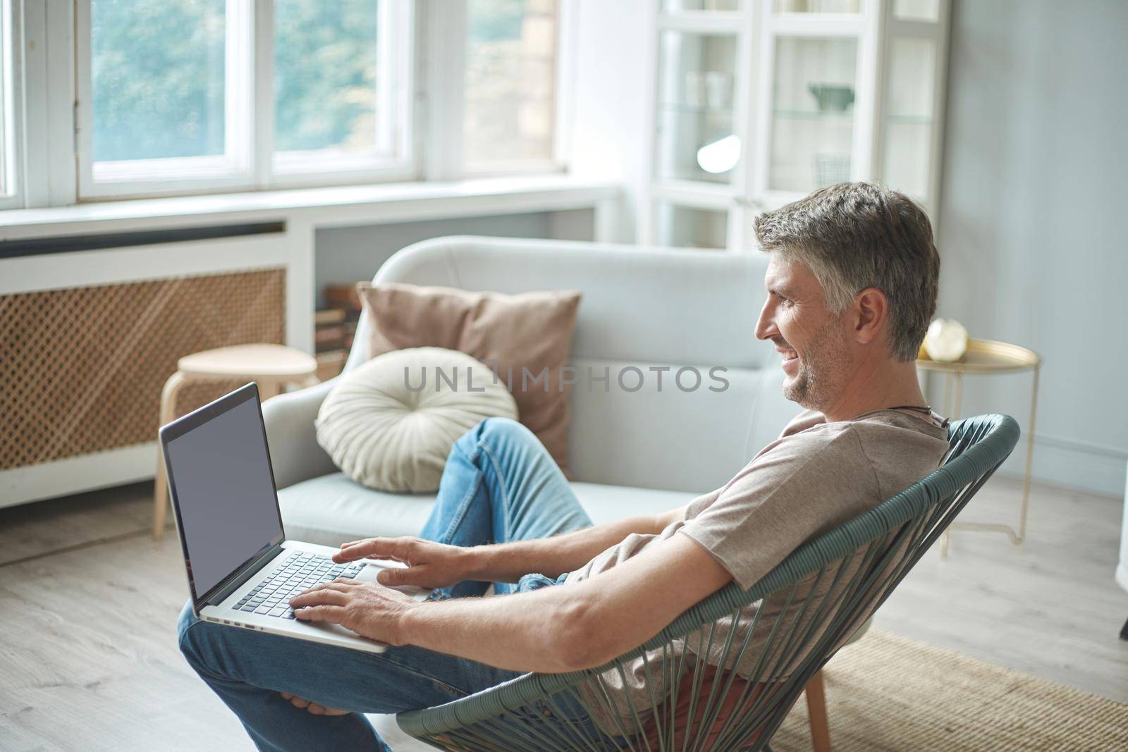 cropped image of a man using a laptop while sitting in a chair. side view.