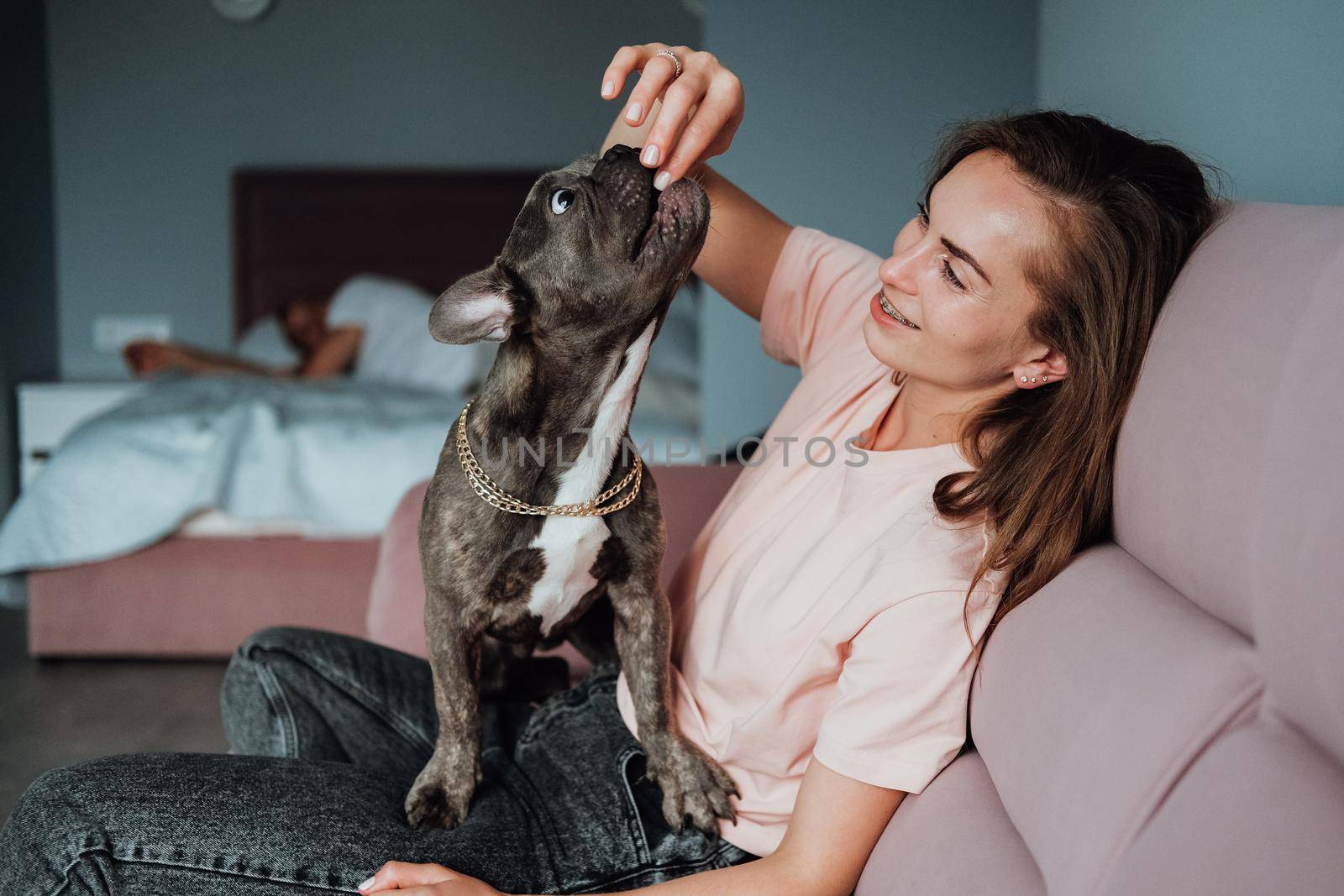 Young Caucasian Woman Playing with Her Pet at Home, Small French Bulldog Eating from Owner's Hand
