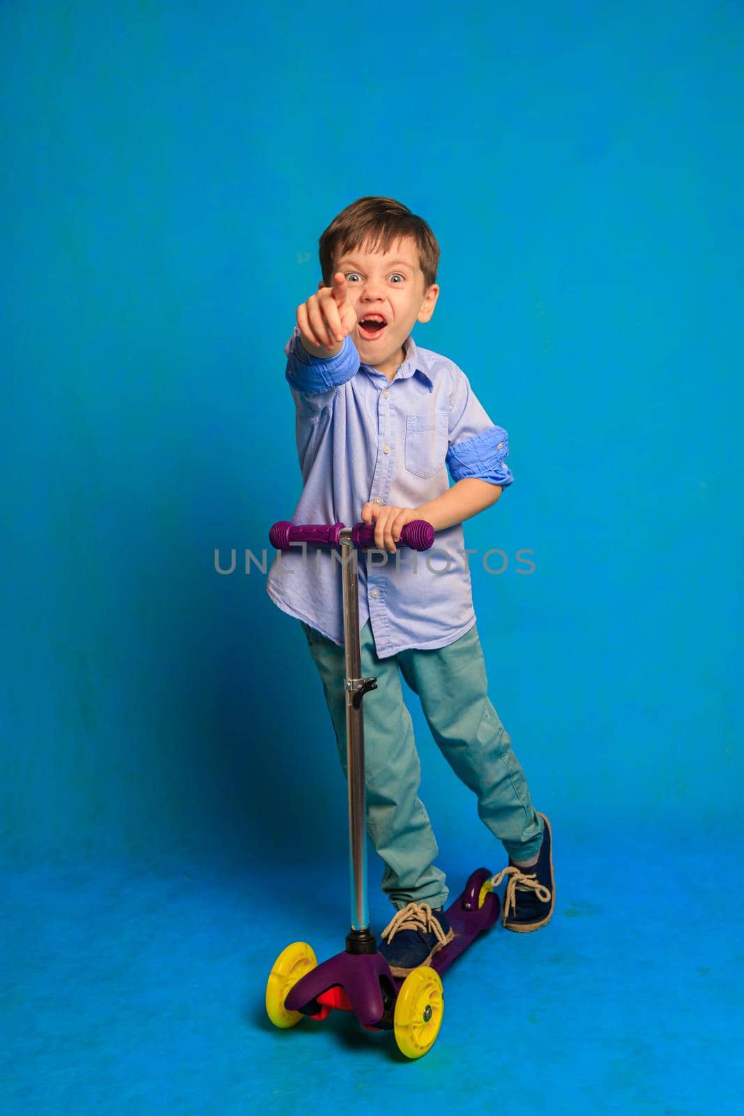 A boy on a scooter on a blue background . An article about children's scooters. An article about the choice of a scooter for a child. A happy child. Blue background and a boy. Copy Space