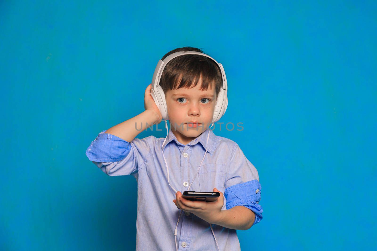 A boy with headphones on a blue background . Children's headphones. Harm of headphones for the child. Useful audiobooks for children. An article about children's leisure. Music. Copy Space