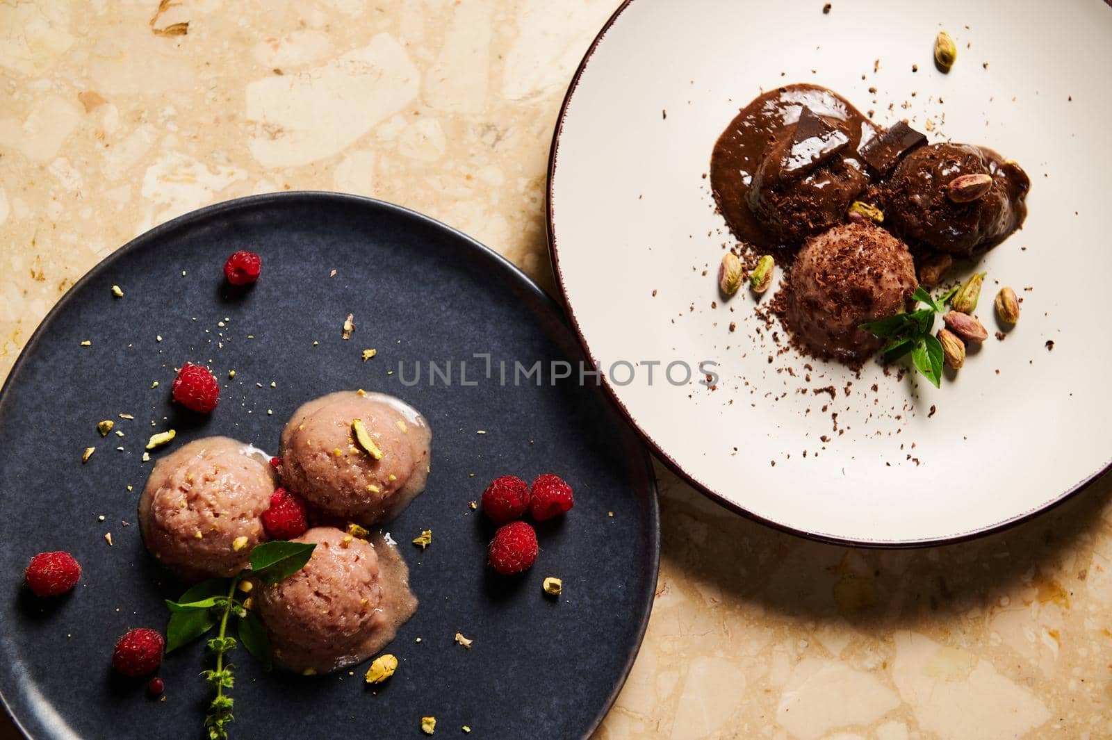Flat lay of ceramic plates with scoops of refreshing raw vegan ice cream, topped with raspberries and lemon basil leaves and chocolate dairy free sorbet, on a marble table background. Food still life