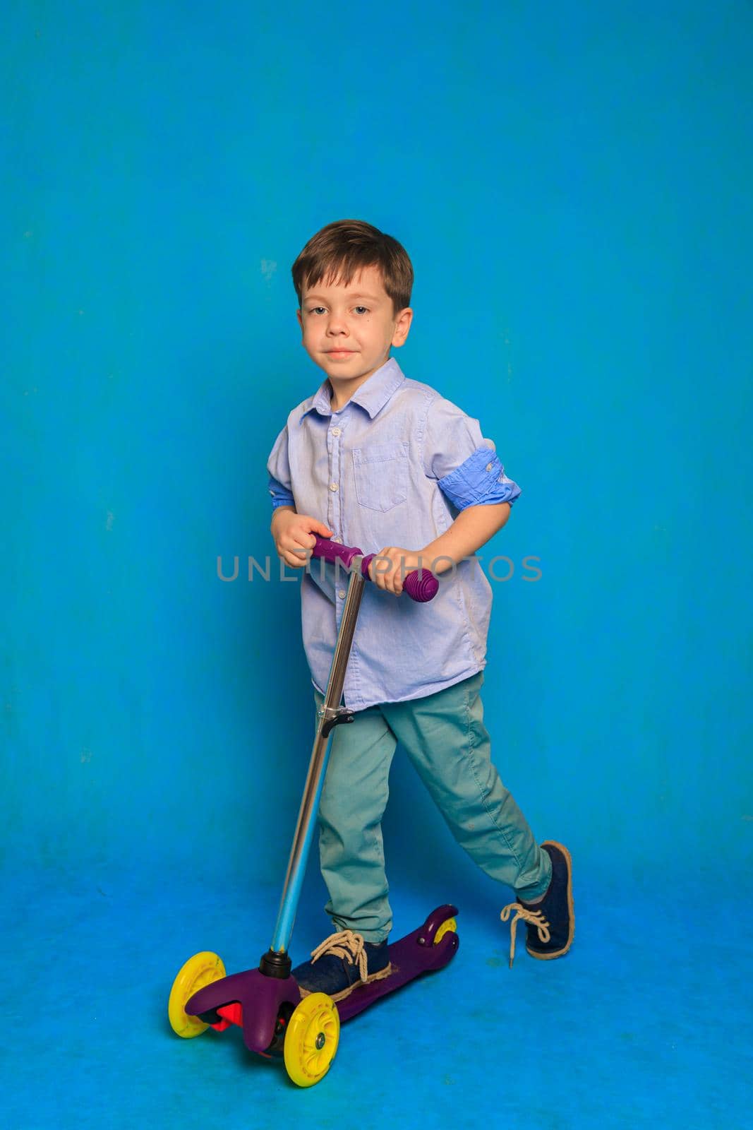 A boy on a scooter on a blue background . An article about children's scooters. An article about the choice of a scooter for a child. A happy child. Blue background and a boy. Copy Space