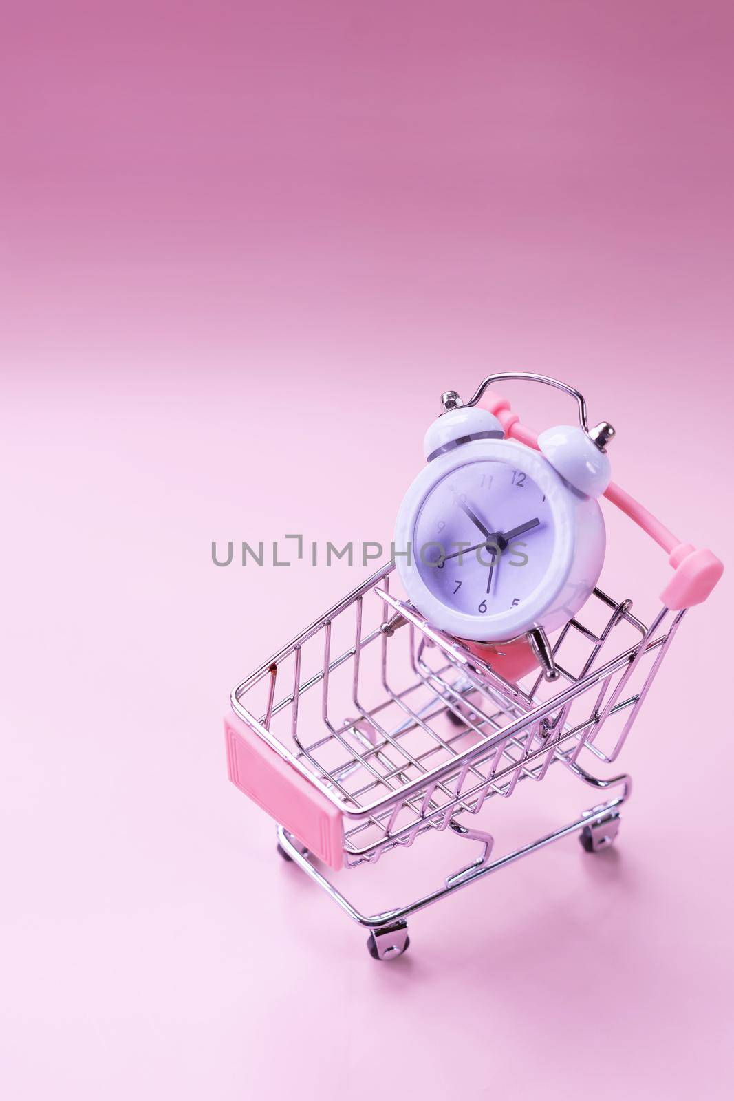 Black alarm clock and toy shopping cart isolated on white. watch in the shopping cart, lack of time, waste of time, shopping time.