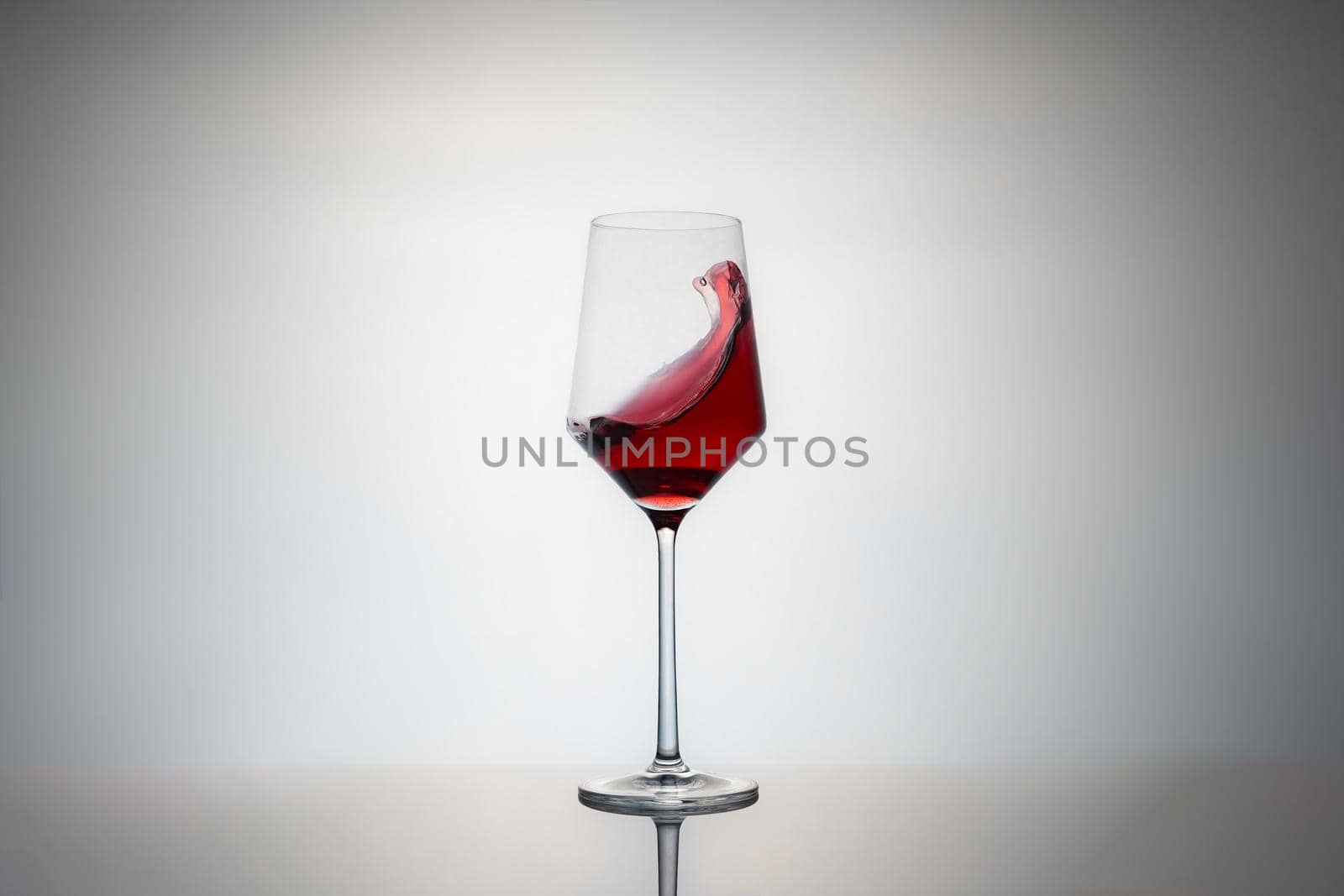 movement of a crystal glass full of red wine. red wine glass isolated on grey background with reflection on the base and vignetting. image to crop. Hard ligth