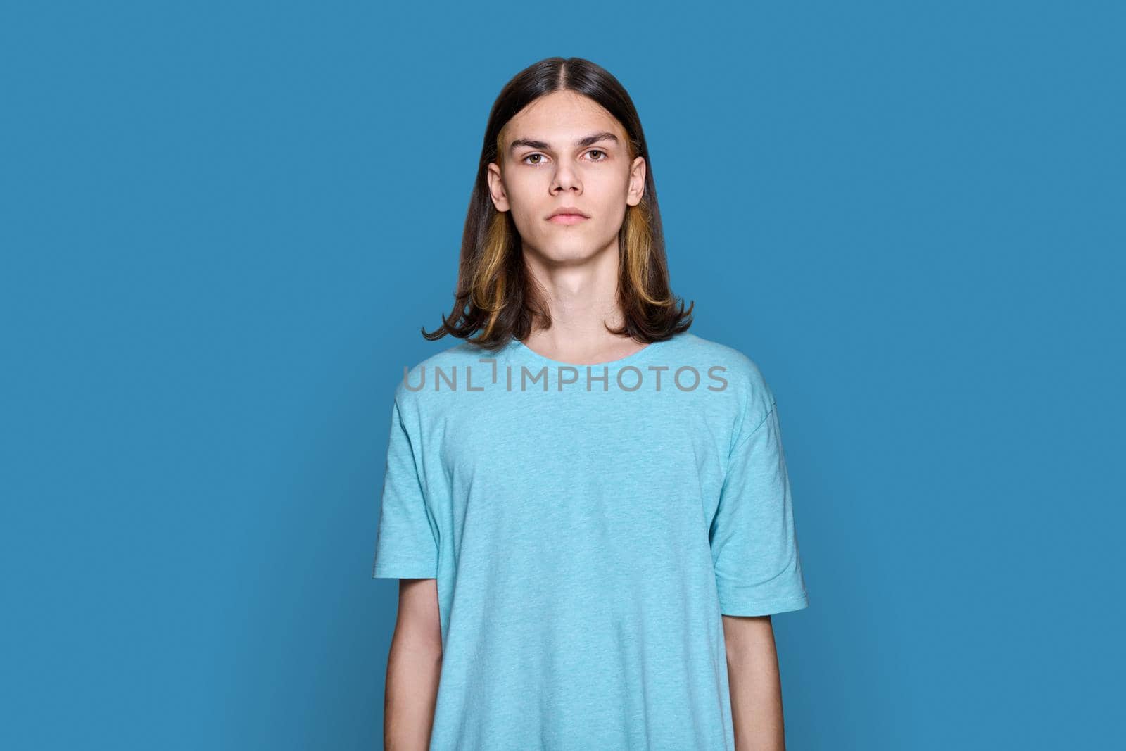 Portrait of serious teenage guy looking at camera on blue background by VH-studio