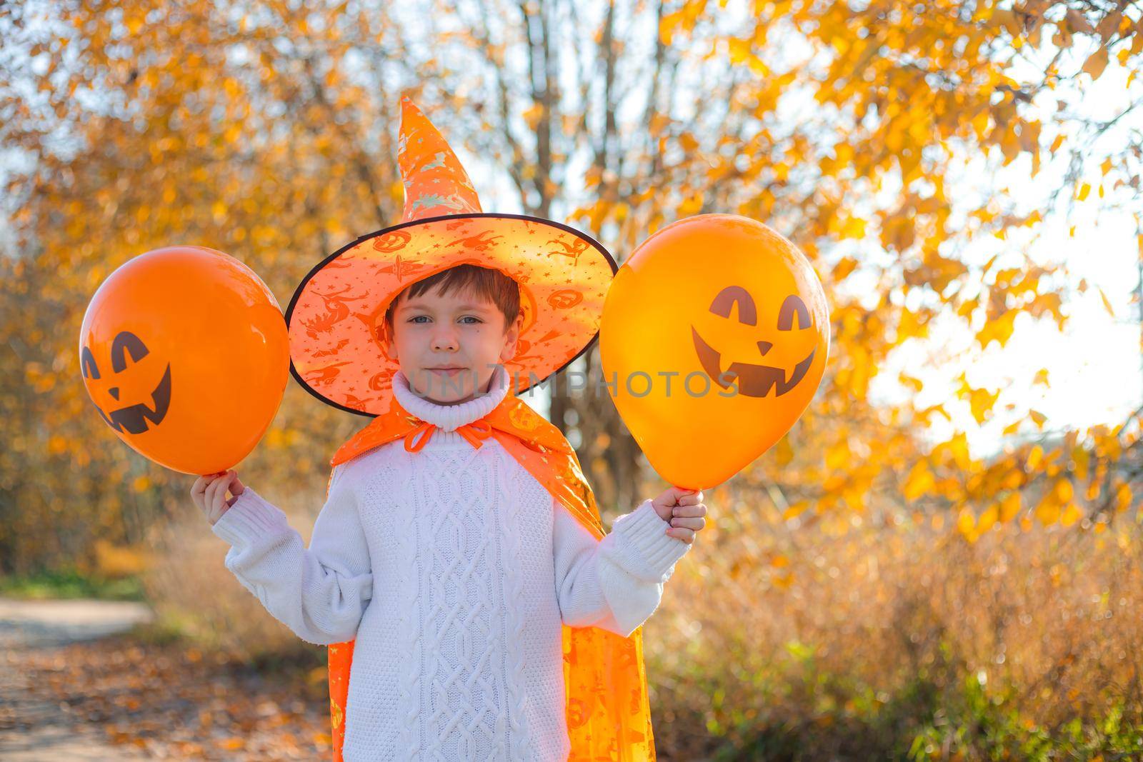 Portrait of a boy in Halloween clothes with pumpkin balloons on the street . A traditional holiday. October 31. Autumn Holiday