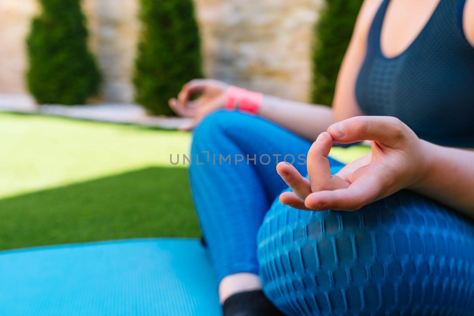 cropped shot of a young woman doing yoga, lotus position, on a mat in the garden. unrecognisable woman doing meditation and breathing exercises. concept of health and well-being. natural light in the garden.