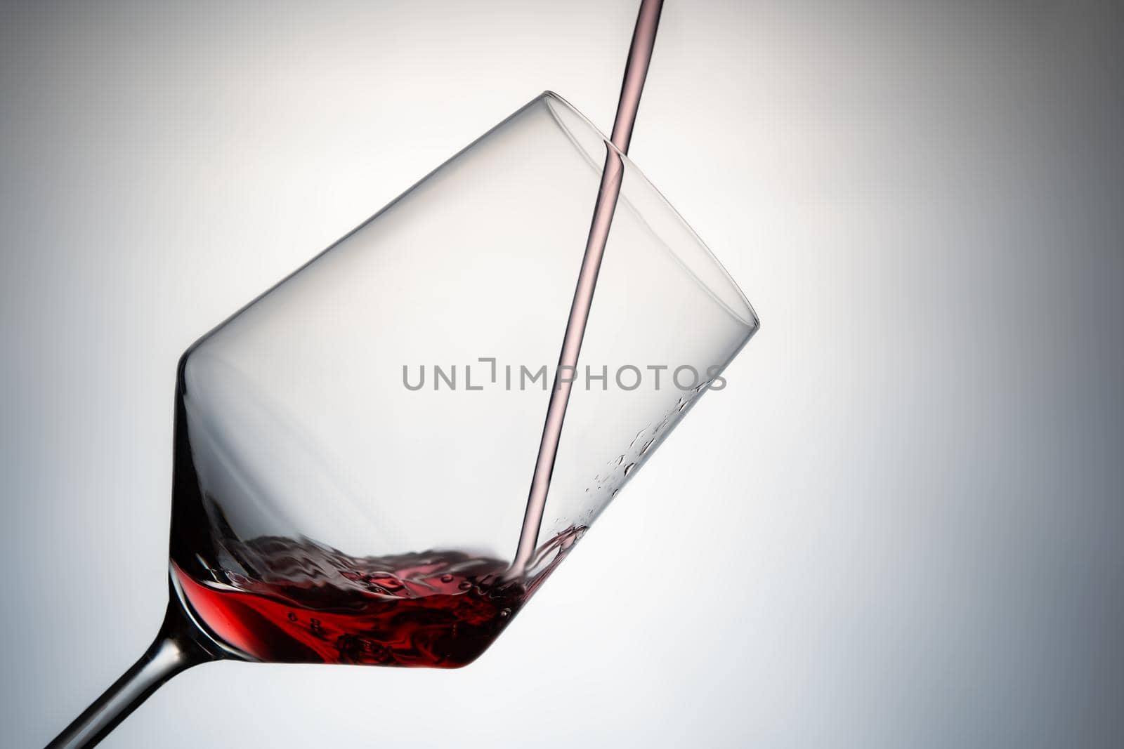 close-up of filling a crystal glass with red wine. pouring red wine into a crystal glass isolated on a grey background. image to cut out. concept drinks. Hard ligth