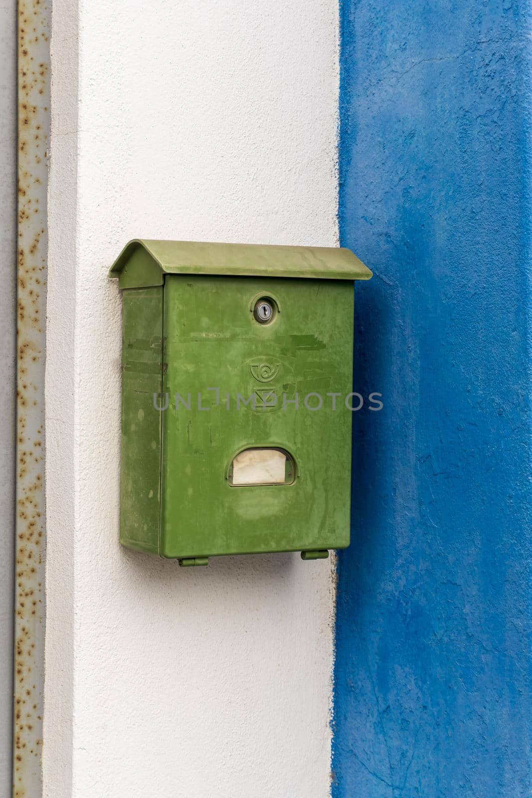 Old green mailbox on the white and blue wall of the house close up