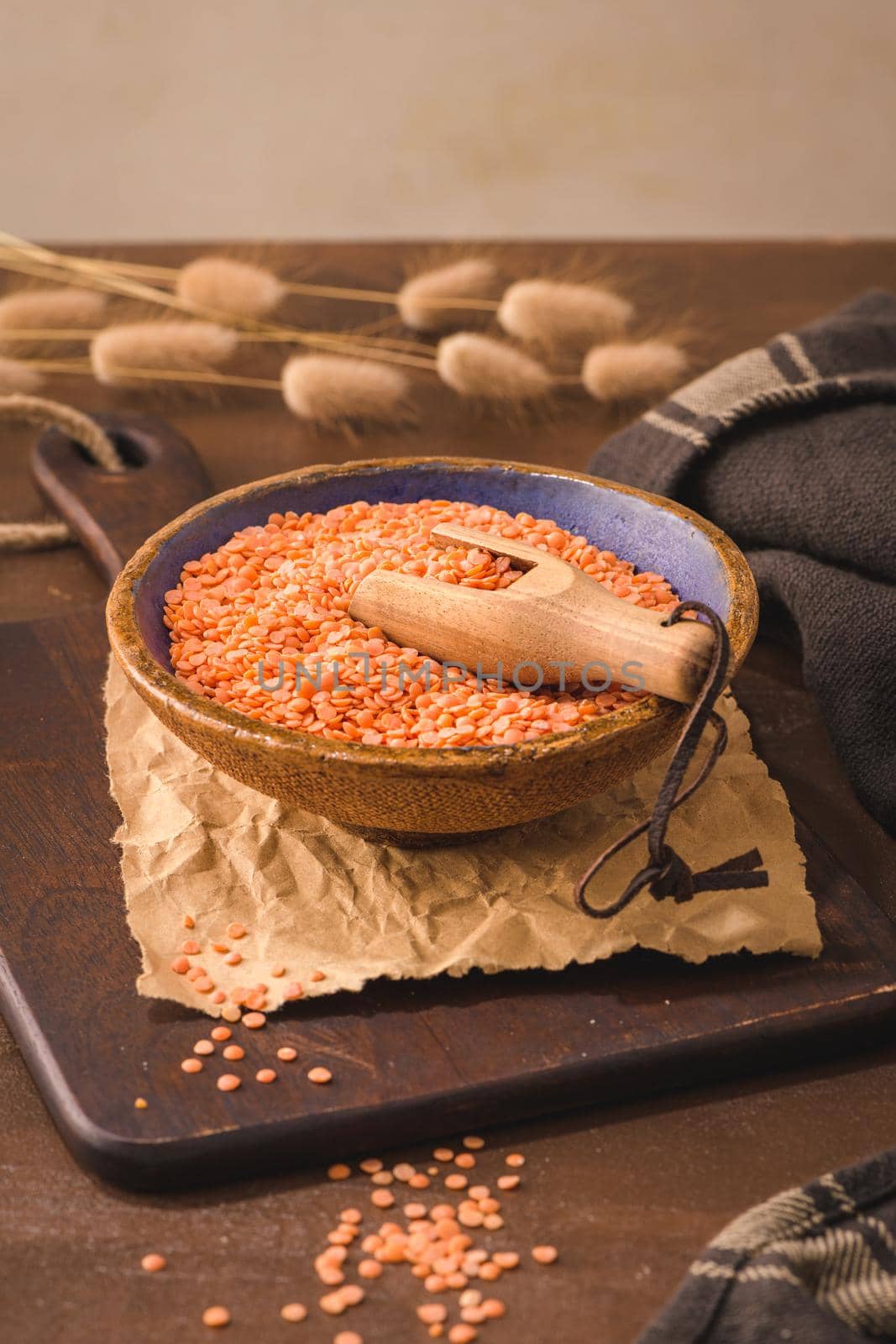 Red lentils in a ceramic bowl with a wooden scoop on a kitchen countertop.