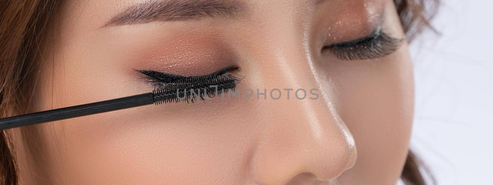 Closeup gorgeous young woman putting black mascara on her eyelashes with brush. by biancoblue