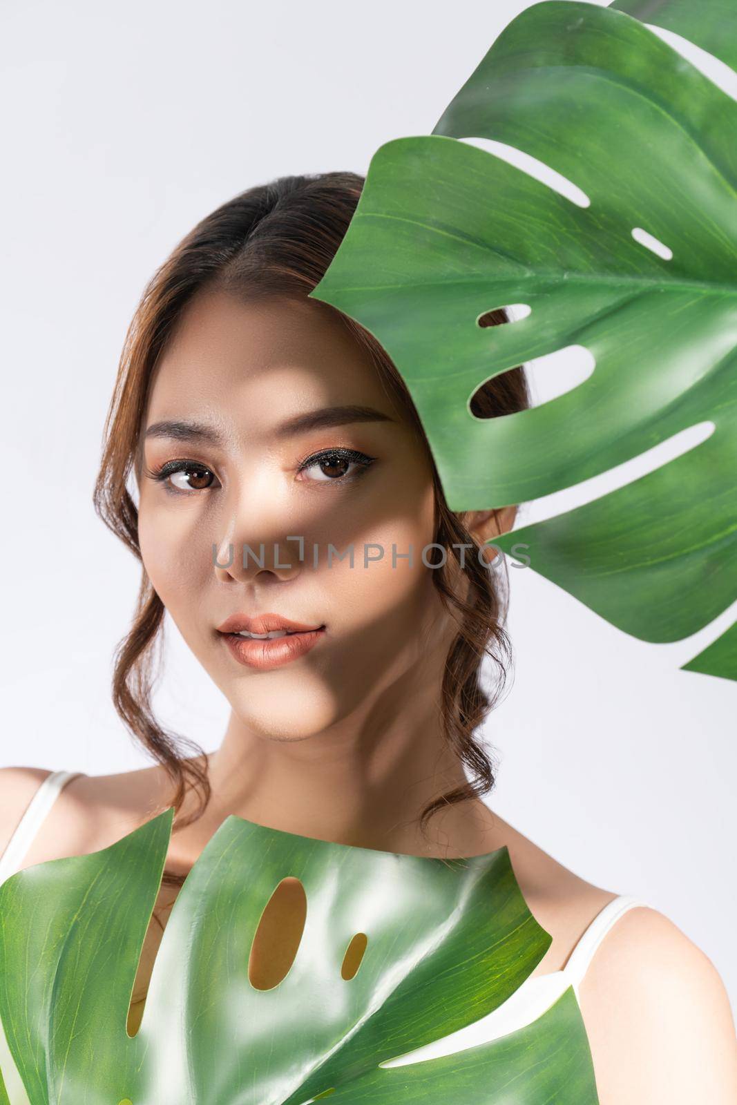 Closeup young gorgeous woman with healthy skin holding green leaf near her face. by biancoblue