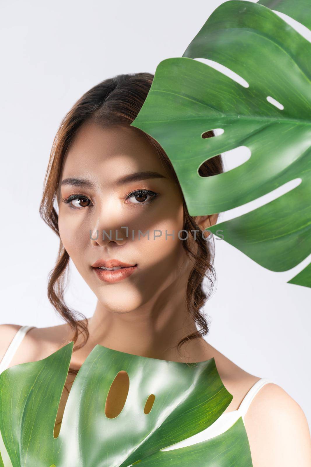 Closeup portrait of young gorgeous woman with healthy fair skin holding big green leaf near her face. Skin care beauty care concept.