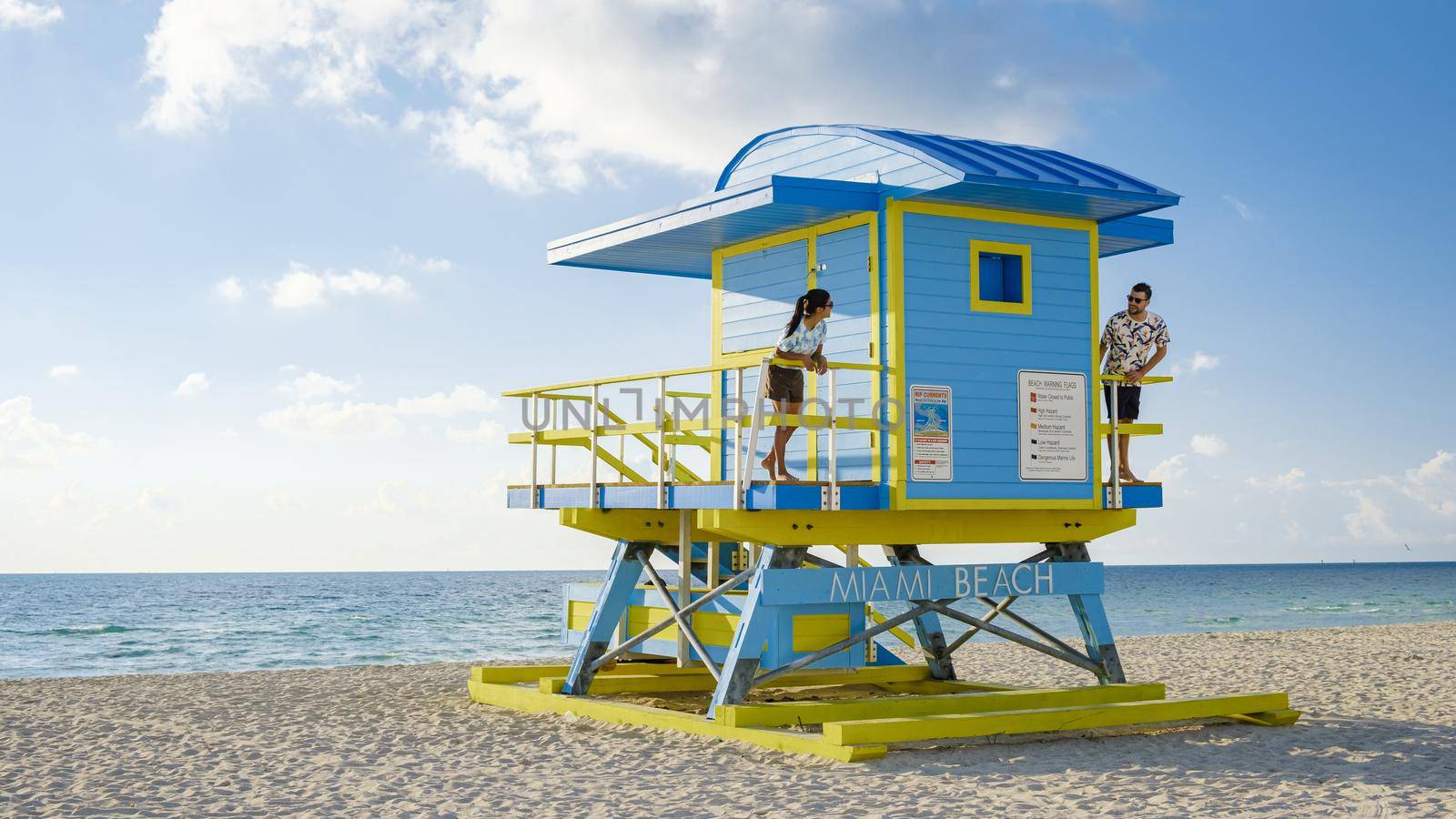 Miami Beach, a couple on the beach in Miami Florida, lifeguard hut Miami Asian women and caucasian men on the beach during sunset. man and woman relaxing at a lifeguard hut looking at ocean