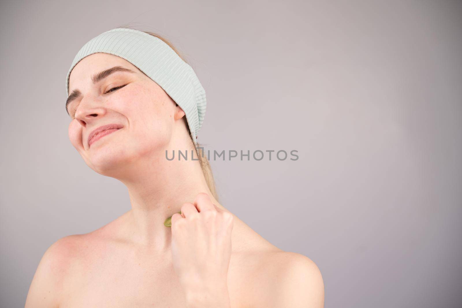 Portrait of a young woman massages her face with a gouache scraper on a white background