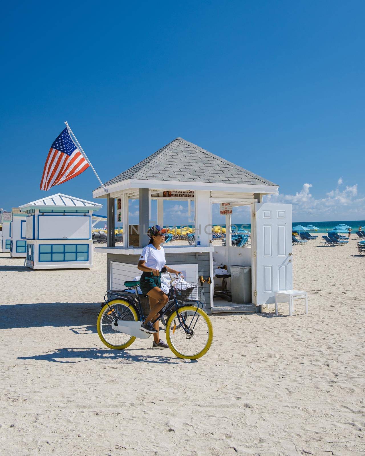 Young women on the beach Miami with a bicycle, colorful Miami beach, and a Lifeguard hut in South Beach, Florida. Asian women bicycle on the beach