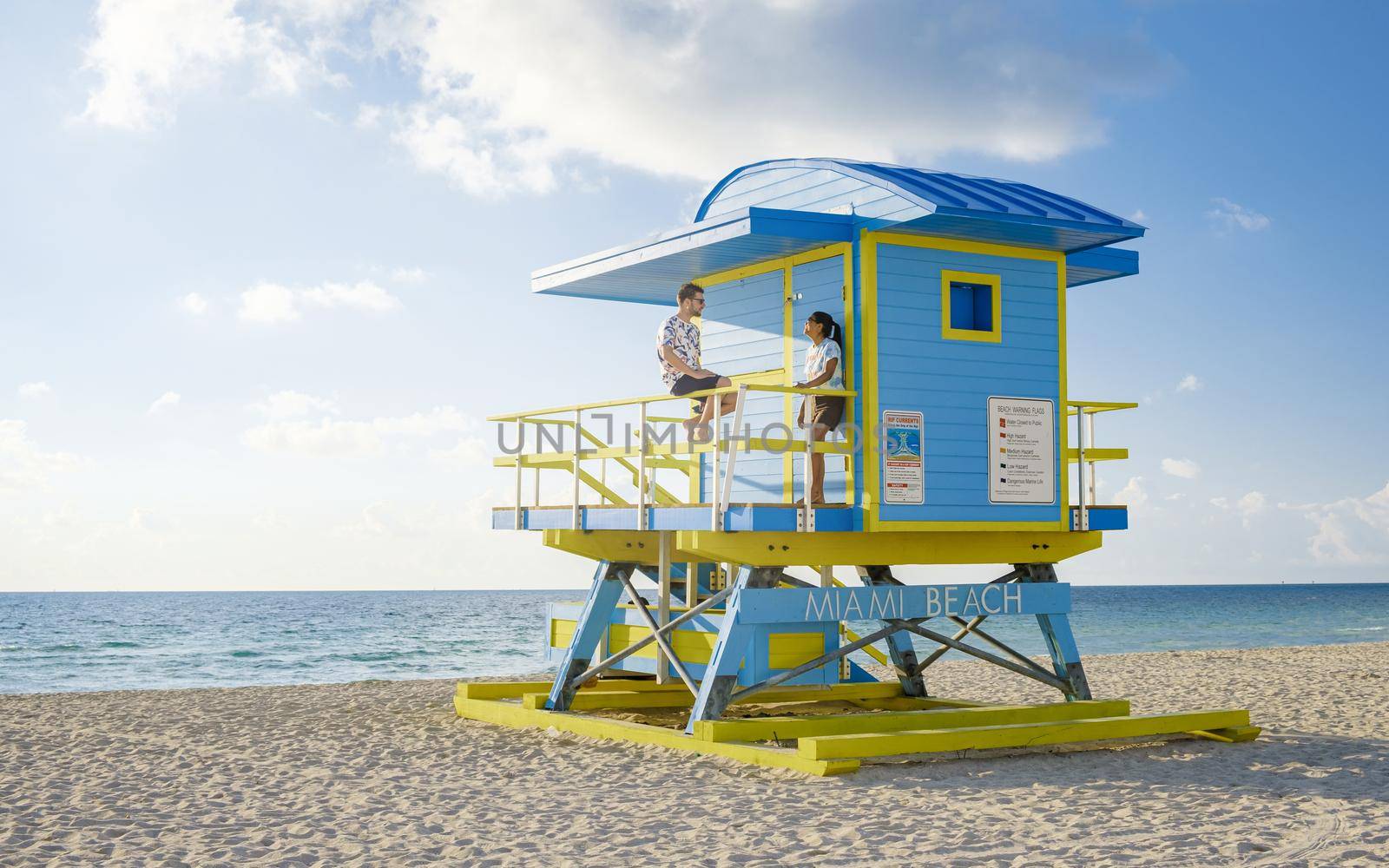 Miami Beach, a couple on the beach in Miami Florida, lifeguard hut Miami Asian women and caucasian men on the beach during sunset. man and woman relaxing at a lifeguard hut looking at ocean