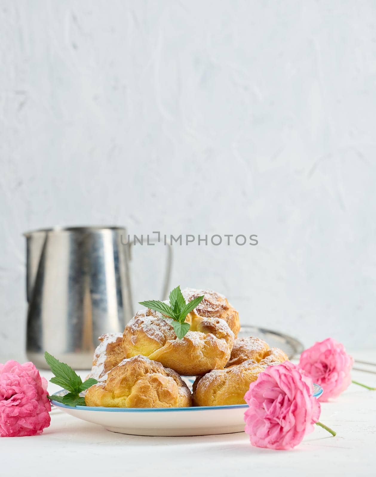 Baked eclairs with custard cream on a metal round plate sprinkled with powdered sugar