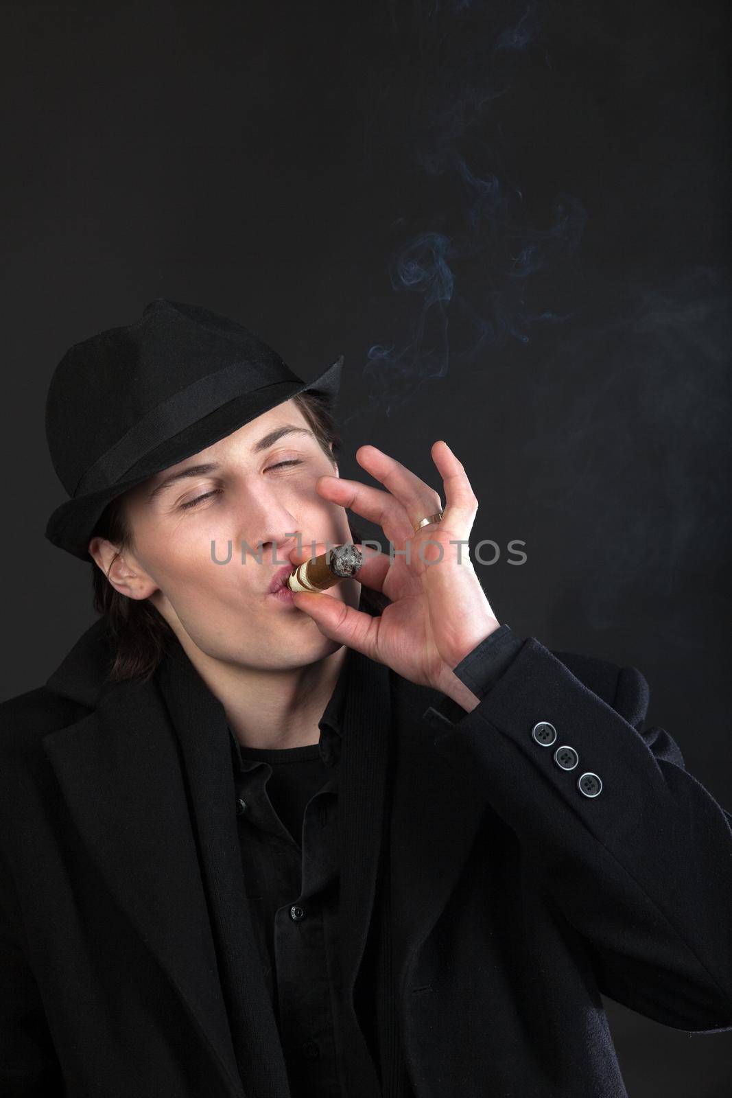 Man in black cloth and hat smoke cigar by rivertime