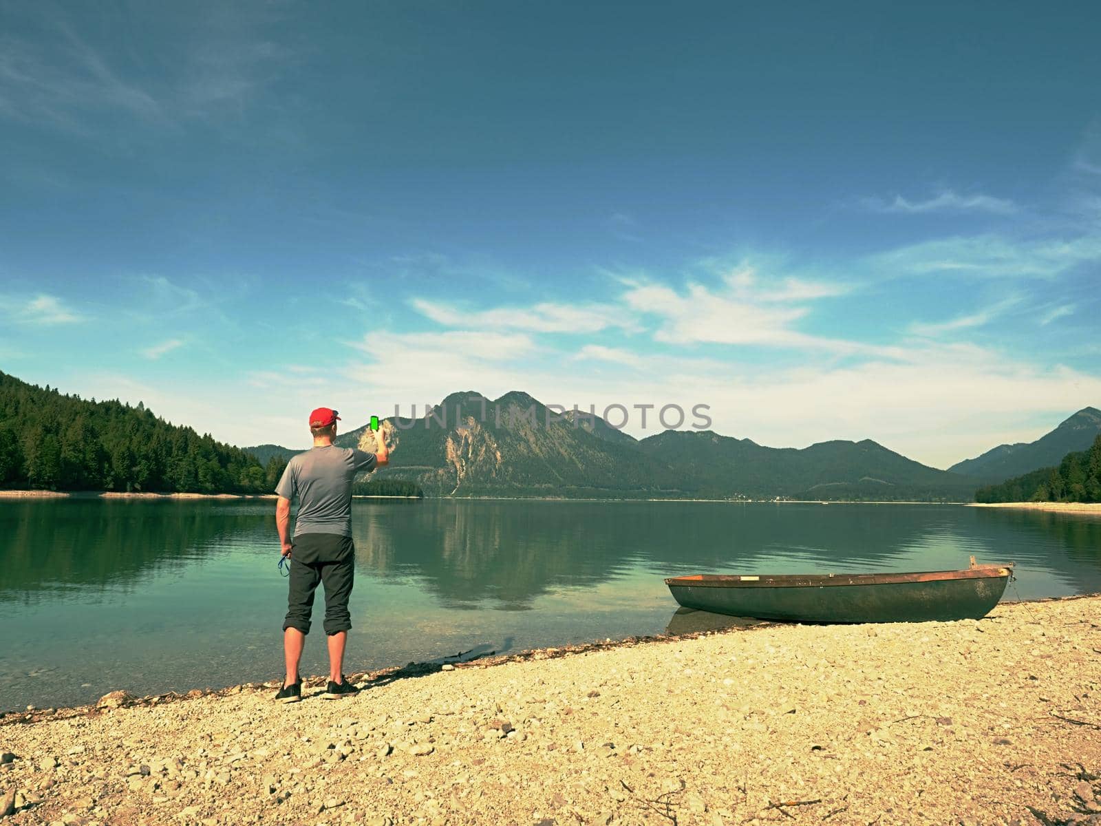 Photo traveler is taking memory photo of lake scenery. Blue lake between high mountains, peaks touch in blue sky. Travel lifestyle concept