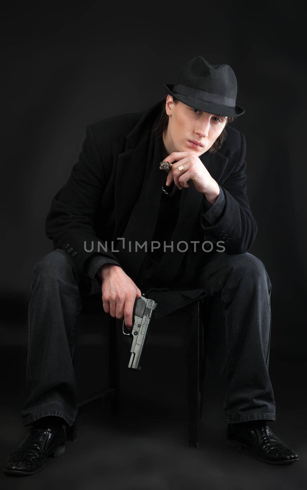 Man with pistol sit in black cloth look at you