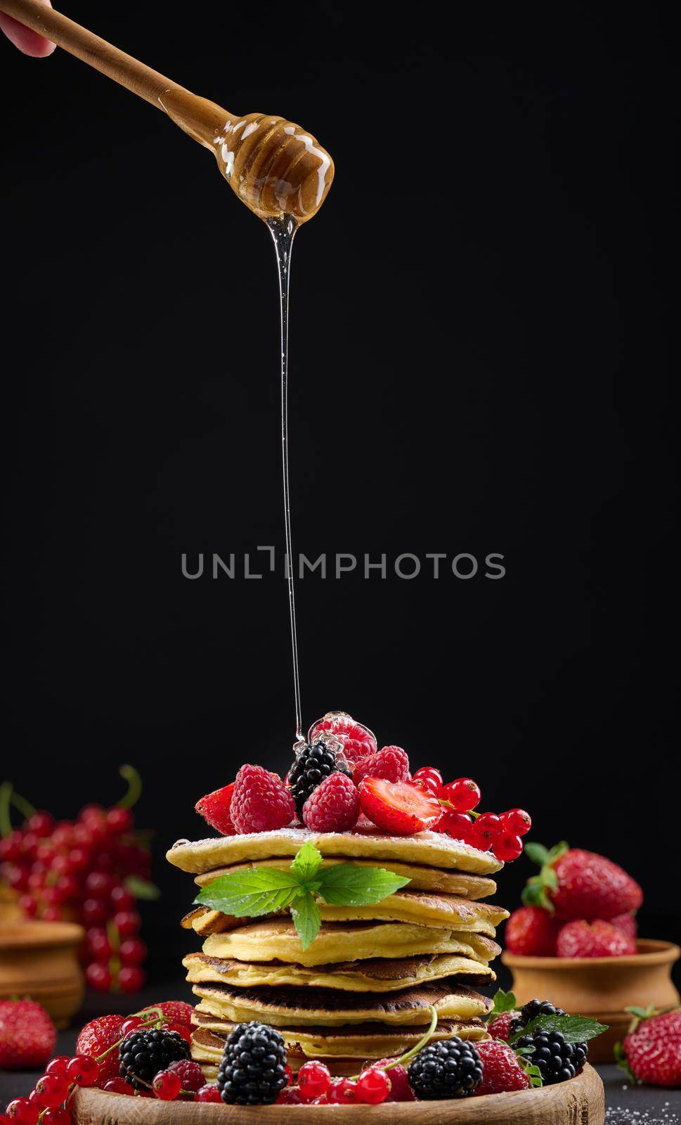 Stack of pancakes with fresh fruit sprinkled with honey on a black background