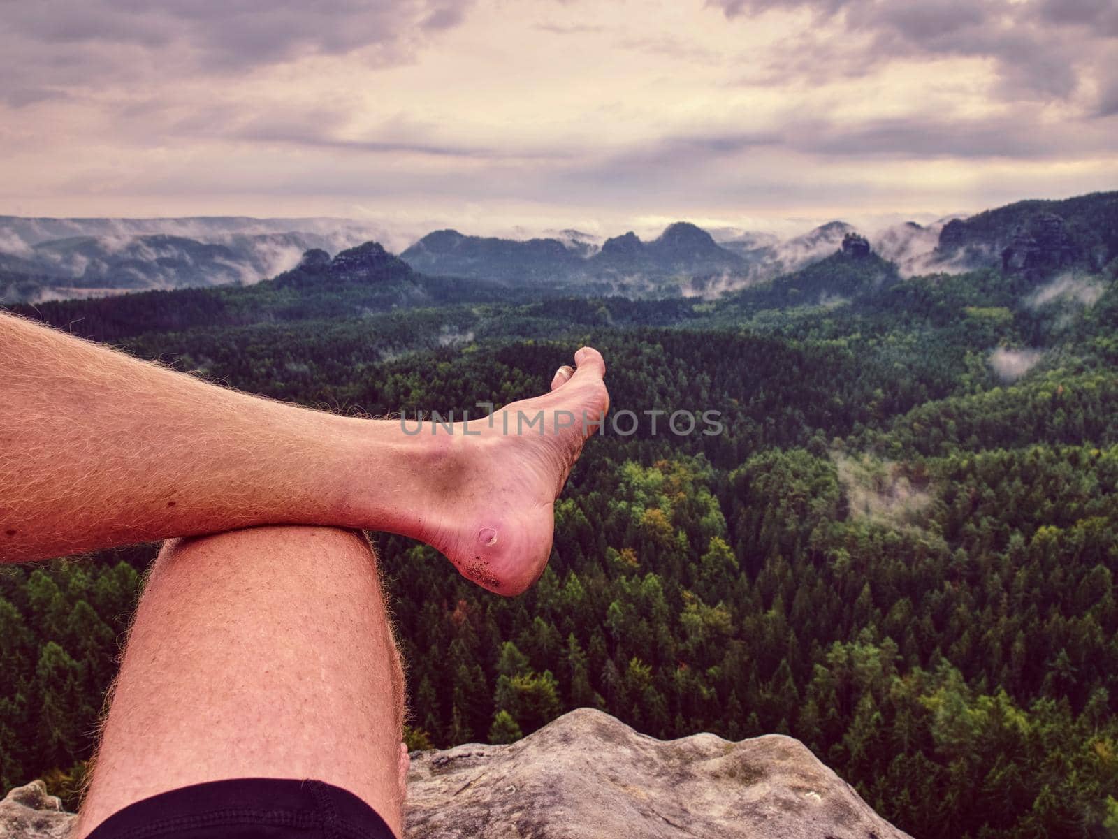 First person perspective shot from hiker sit at edge of cliff above rain forest valley